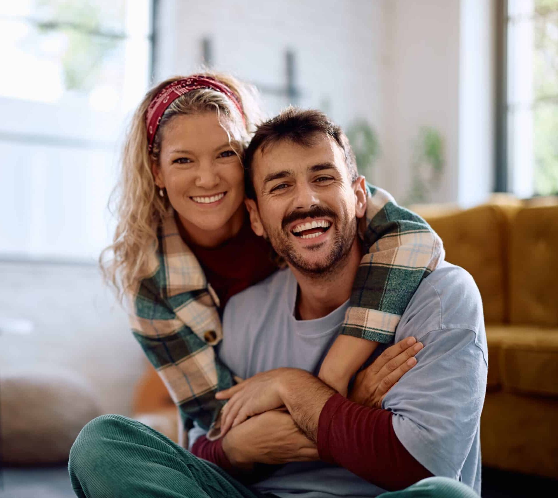 Happy,Embraced,Couple,Relaxing,At,Home,And,Looking,At,Camera.